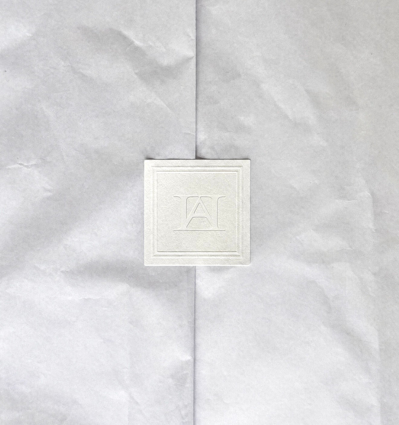 Ivory tissue paper folded open around a square seal blind-embossed with the AFTERHOURS monogram